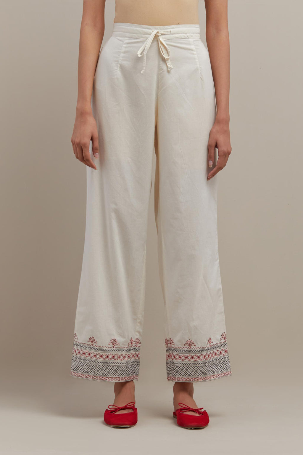 Off white straight pants with quilted embroidery at bottom hem.