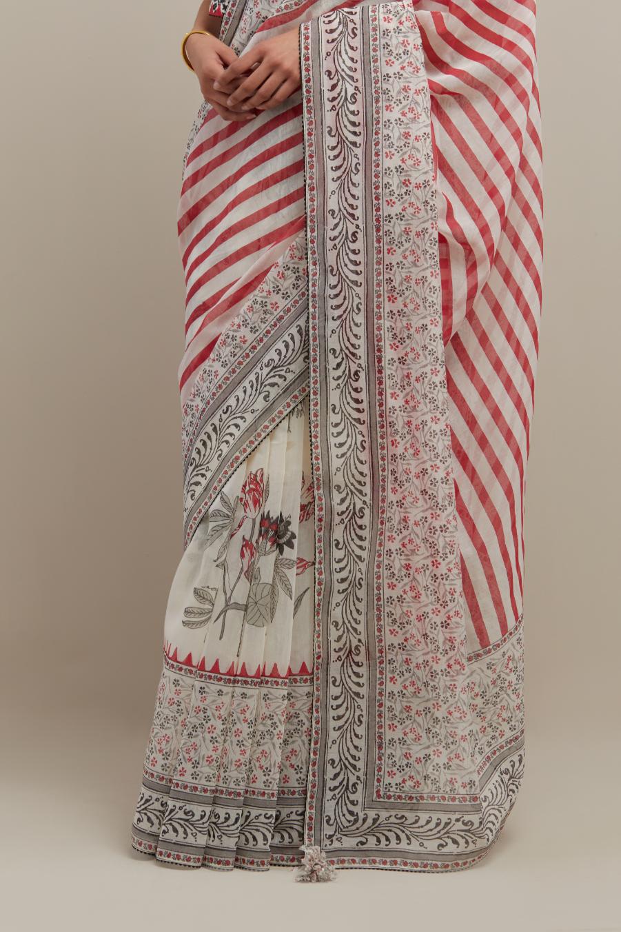 Off white cotton chanderi saree, highlighted with all-over bold stripe and floral hand block print, paired with off-white hand block printed cotton blouse, paired with off-white cotton blouse with all-over red & black hand block print.