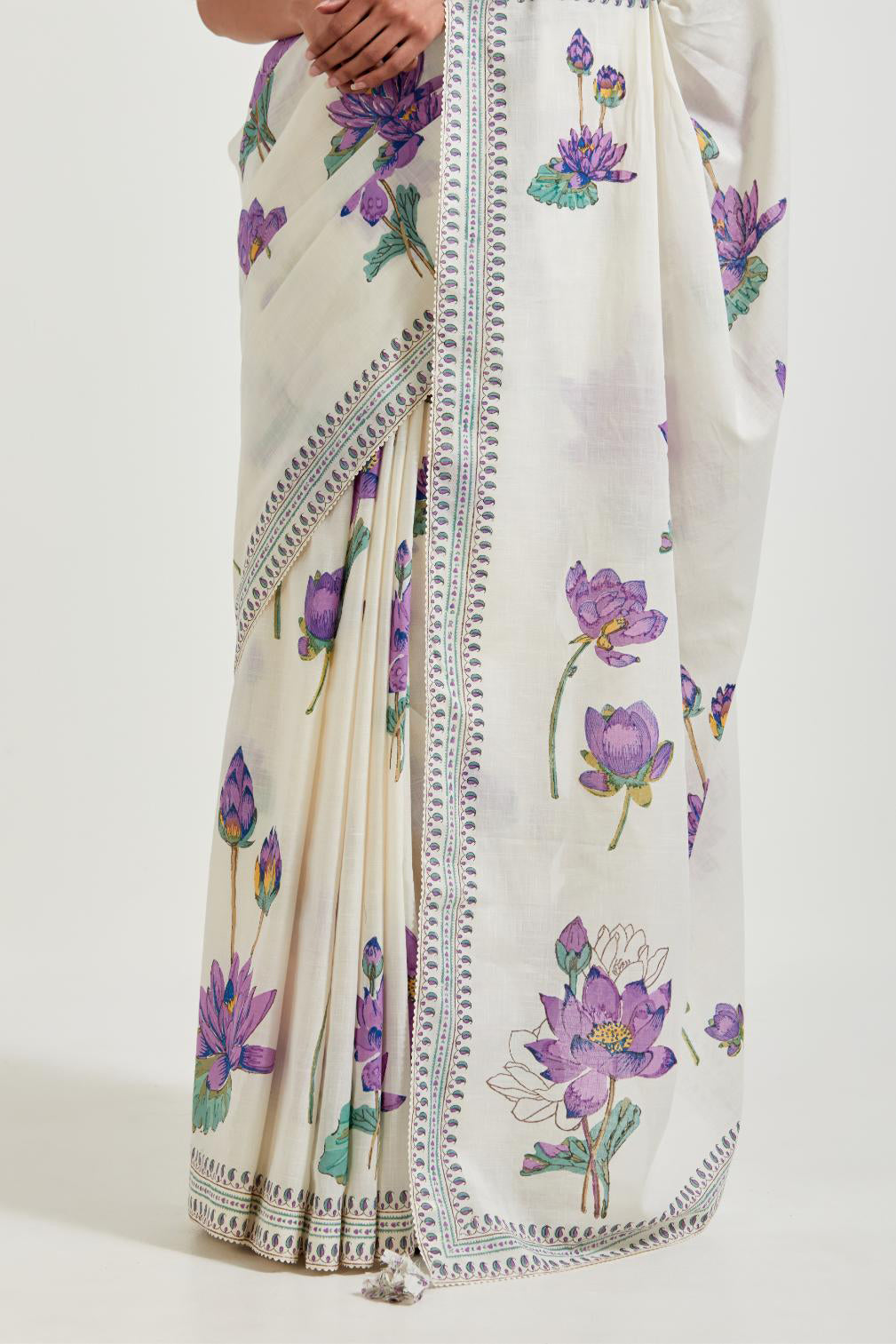 Off white cotton saree, highlighted with all-over purple & green lotus flower hand block print, paired with off-white cotton blouse with all-over purple & green small lotus flower hand block print.